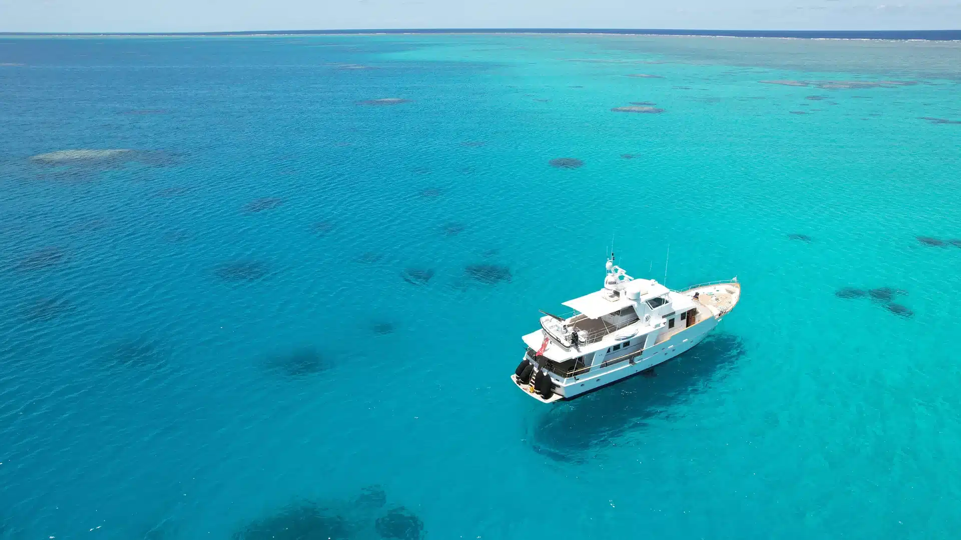 Everycharteratlanticprincess | atlantic princess | atlantic princess White motor yacht anchored in clear turquoise sea with shallow reefs visible around it